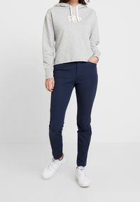 Sudadera gris corta con el logotipo de GAP, combinada con pantalones ajustados azul marino y zapatillas blancas, con una textura de tela suave.