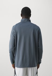 Gray long-sleeve pullover with a high collar, featuring smooth texture and raglan sleeves. The fabric appears lightweight and athletic.