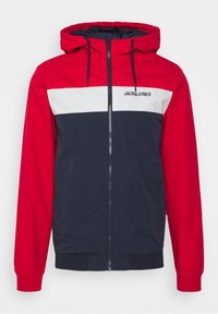 Rød, hvid og marineblå hættejakke med lynlås. Har et logo på brystet, elastiske manchetter og sidelommer. Glat tekstur, sporty design.