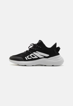 Black mesh sneaker with a textured finish, white branding, and a padded collar. Features a chunky white sole and black laces.