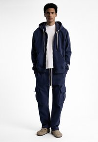 Hoodie en fleece bleu marine avec cordons de serrage et poches avant, associé à un pantalon cargo assorti avec poches latérales et poignets élastiques.