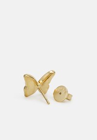 Boucles d'oreilles en forme de papillon en or avec une finition polie, comportant un tige droite et un dos en métal rond gravé "GUESS."