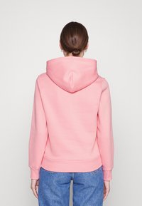 Felpa rosa con un design aderente, cappuccio a doppio strato, polsini e orlo a coste, e texture liscia. Indossata con jeans blu.