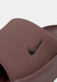 Καφέ συνθετικό σανδάλι σαγιονάρας με υφή στην επάνω όψη, διαθέτει μαύρο λογότυπο Nike swoosh και φαρδιά σχεδίαση ιμάντα.