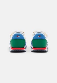 Des baskets multicolores présentent une tige blanche avec des accents bleus, verts, jaunes et rouges. Le talon texturé et la semelle en caoutchouc assurent une bonne adhérence.