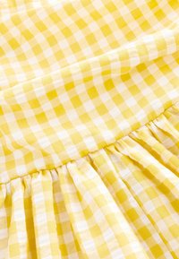 Tessuto a quadri giallo e bianco con dettaglio di cucitura arricciata, che mostra la texture e il motivo a scacchi su una superficie tessile morbida.