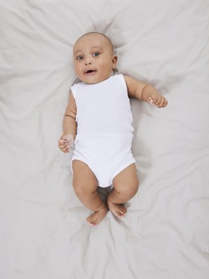 Un body sin mangas blanco en un bebé, acostado sobre una superficie texturizada de un beige claro; con extremidades cortas y una cabeza redonda, ojos marrones y una expresión neutral.
