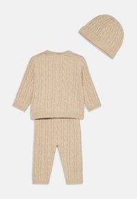 Bežový sveter s pleteným vzorom a ladiace nohavice, obe s rebrovanými manžetami. Doplněné o priliehavú pletenú čiapku v rovnakej farbe.