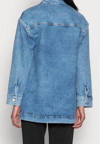 Light blue denim jacket with long sleeves, front pockets, and buttoned cuffs. Distressed texture and relaxed fit. Back view shown.