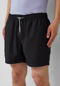 Zwarte zwembroek met een trekkoord in de taille, voorzien van een elastische band en een gladde textuur. Ontworpen voor comfort en gemak tijdens het dragen.