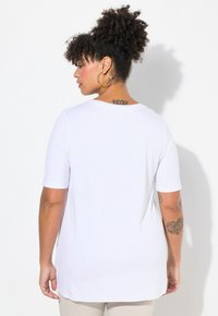 Camiseta blanca de manga corta, hecha de tela suave, presenta un cuello redondo y un corte holgado, con un dobladillo trasero más largo.