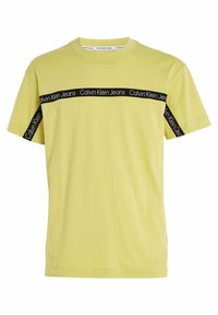 Žluté bavlněné tričko s krátkými rukávy, na hrudi má černý pruh s logem "Calvin Klein Jeans" a na bočním švu.