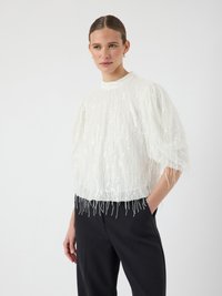 Witte blouse met korte mouwen van textuurstof en franje-details aan de onderrand, gecombineerd met zwarte hoog-waist broek.