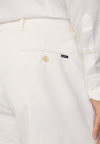 Pantaloni bianchi in cotone con tasca posteriore, dotati di un bottone beige e di un'etichetta nera con la scritta "HACKETT". Tessuto liscio, vestibilità su misura.