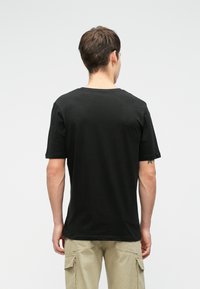 Tricou din bumbac negru cu guler rotund și mâneci scurte, având o textură netedă și o croială lejeră, prezentat din spate.