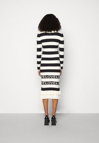 Raidallinen neulemekko musta-valkoisena, jossa on pitkät hihat, röyhelöhelma ja nauha, jossa on suurilla kirjaimilla teksti "LOVE".