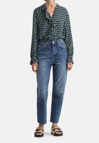 Blusa a maniche lunghe con un motivo circolare verde, bianco e blu navy, colletto a strati con rouches; jeans blu a vita alta; sandali neri.