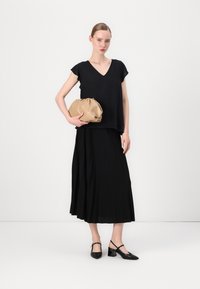 Svart kortermet topp med V-hals, kombinert med en plisséd svart skjørt. Beige clutch-veske med en samlet design og svarte blokkhelsesko.
