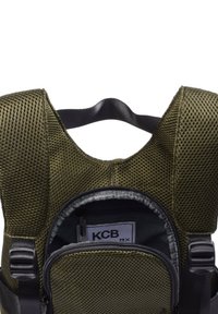 Mochila de malla verde oliva con correas acolchadas, bolsillo frontal con cremallera y cremallera negra. El interior cuenta con una etiqueta y compartimentos de almacenamiento adicionales.