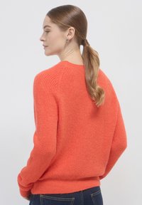 Korallenfarbener Strickpullover mit einem strukturierten, gerippten Muster, Raglanärmeln und einer lockeren Passform. Mit Rundhalsausschnitt und gerippten Bündchen.