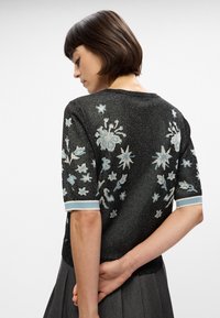 Μαύρο πουλόβερ με κεντημένα σχέδια και ανοιχτό μπλε λεπτομέρειες. Διαθέτει γυαλιστερή υφή, κοντά μανίκια και λουλουδάτα αστέρια στο πίσω μέρος.