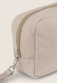 Borsa in tela beige con superficie texturizzata, cerniera dorata e tracolla staccabile. Presenta una forma rettangolare e un dettaglio di cucitura sottile.