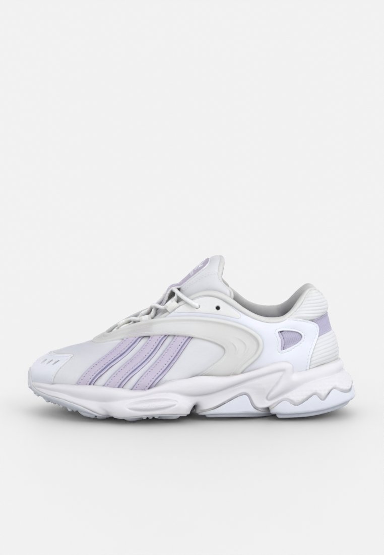 Scarpa sportiva bianca con dettagli viola, caratterizzata da una parte superiore testurizzata, lacci ben in evidenza e un design della suola spessa e ondulata per stabilità.