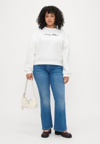 Hvid sweatshirt med "Tommy Hilfiger" logo, blå flagrende jeans, sorte platform sko og en lille hvid håndtaske.