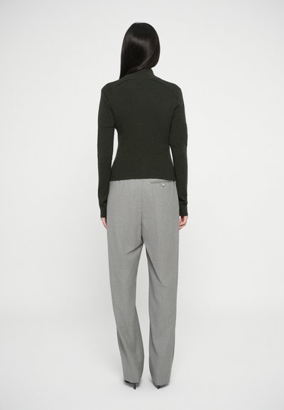 Σκούρο πράσινο εφαρμοστό πουλόβερ με ψηλό γιακά και μακρύ μανίκι, συνδυασμένο με ανοιχτό γκρι παντελόνι φαρδιάς γραμμής που διαθέτει πίσω τσέπη.
