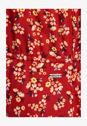 Červená látka s květinovým vzorem, obsahující žluté, bílé a modré květiny. Obsahuje malou obdélníkovou visačku Big Star.