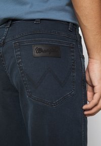 Vaqueros azul oscuro con corte recto. Presentan un parche de cuero en el bolsillo trasero y un pespunte en contraste en un patrón en zigzag.