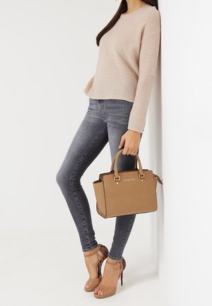 Bolso de mano marrón con asas y detalles dorados, suéter de punto rosa claro, jeans ajustados grises y sandalias de tacón beige con tiras.