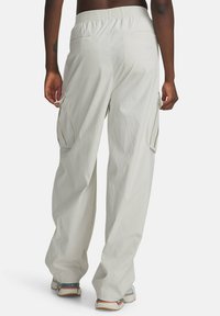 Persona usando pantalones cargo de color beige claro con cinturilla elástica y zapatillas, vista desde la parte posterior sobre un fondo blanco.