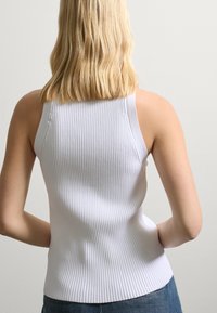 Witte geribbelde tanktop met een aangesloten ontwerp, voorzien van brede schouderbanden, een gladde textuur en een lichte flare aan de onderkant.