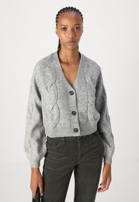 Grå kabelstrikket cardigan med v-hals, fem knapper og ballongsleeves. Bært over olivengrønne kordfløyelsbukser.