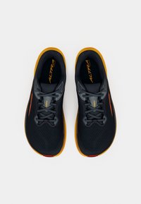 Zwarte hardloopschoenen met een ademend mesh bovenwerk, grijze accenten, oranje logo en een gele rubberen zool, voorzien van platte veters en een gestructureerd ontwerp.