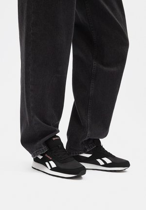 Czarne buty sportowe z białymi akcentami i teksturowaną cholewką, zestawione z luźnymi czarnymi spodniami dżinsowymi, prezentujące swobodny look.