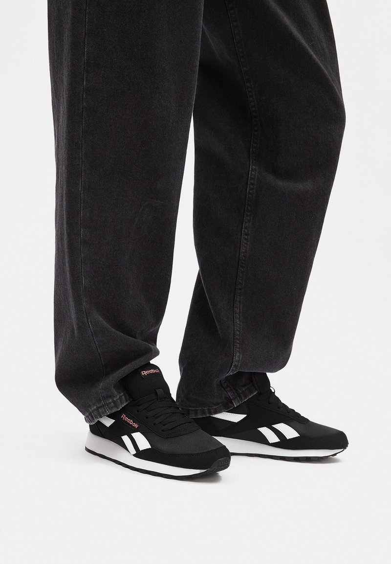 Czarne buty sportowe z białymi akcentami i teksturowaną cholewką, zestawione z luźnymi czarnymi spodniami dżinsowymi, prezentujące swobodny look.