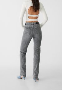 Höga grå jeans med en urtvättad textur, fem fickor och raka ben. Matchas med en vit topp med utskärningar på ryggen.