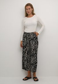 White ribbed long-sleeve top paired with black and white striped wide-leg trousers and black flip-flop sandals.