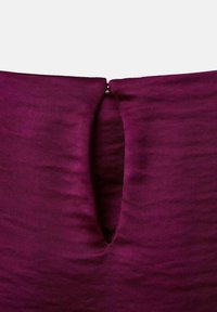 Textil malva con una textura suave que presenta un detalle recortado en el escote, asegurado con un esbelto cierre metálico.
