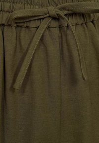 Joggers de tela verde oliva con cintura elástica, detalle de cordón y una trama texturizada. Diseño sencillo sin patrones visibles.