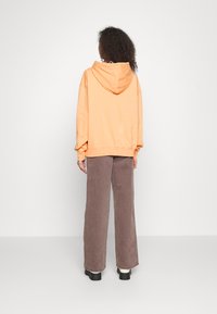 Felpa arancione con cappuccio e vestibilità ampia, con polsini a costine, abbinata a pantaloni a gamba larga in velluto a coste marrone e calzature nere chunky.