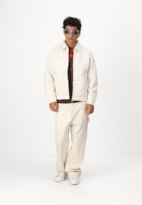 Chaqueta y pantalones de mezclilla blancos con una camiseta gráfica negra debajo. Los accesorios incluyen gafas de sol grises y zapatillas blancas.