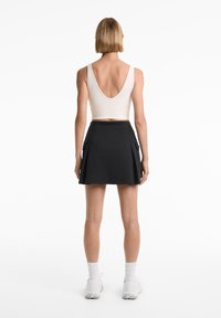 Black pleated skirt with side pockets, paired with a cream V-neck crop top. Model wears white athletic shoes and knee-high socks.