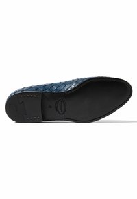 Zapato de cuero tejido azul con suela plana negra, que presenta pequeños acentos metálicos y un logo en la suela. Superficie texturizada con un diseño intrincado.