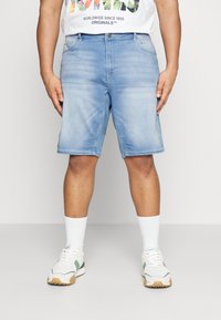 Lichtblauwe denim shorts met een rechte snit, voorzien van vijf zakken en een knoopsluiting. Gecombineerd met witte sokken en sportieve schoenen.