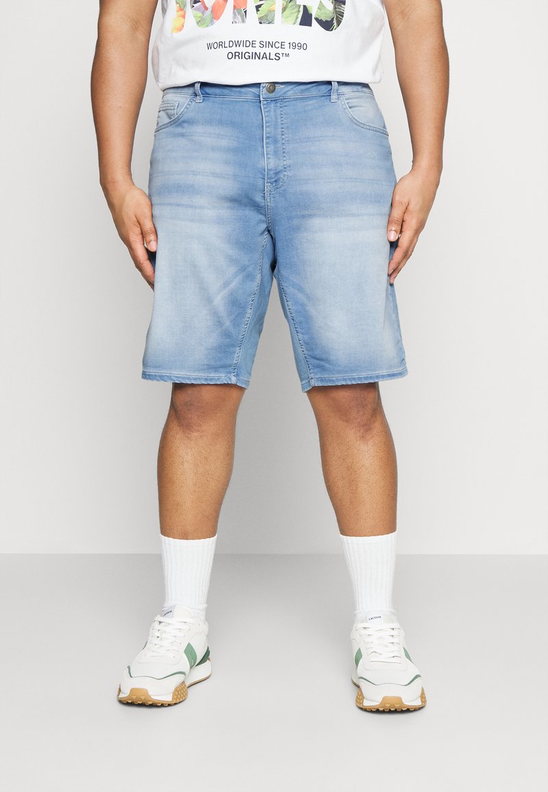 Lichtblauwe denim shorts met een rechte snit, voorzien van vijf zakken en een knoopsluiting. Gecombineerd met witte sokken en sportieve schoenen.