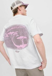 Hvid bomulds T-shirt med en stor pink grafik af træer på ryggen. Korte ærmer, rund hals, afslappet pasform. Komplementeret af en beige mesh kasket.