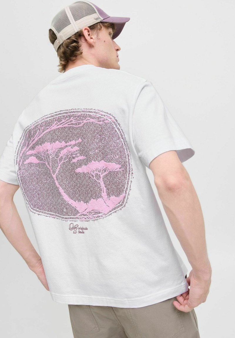 Hvid bomulds T-shirt med en stor pink grafik af træer på ryggen. Korte ærmer, rund hals, afslappet pasform. Komplementeret af en beige mesh kasket.